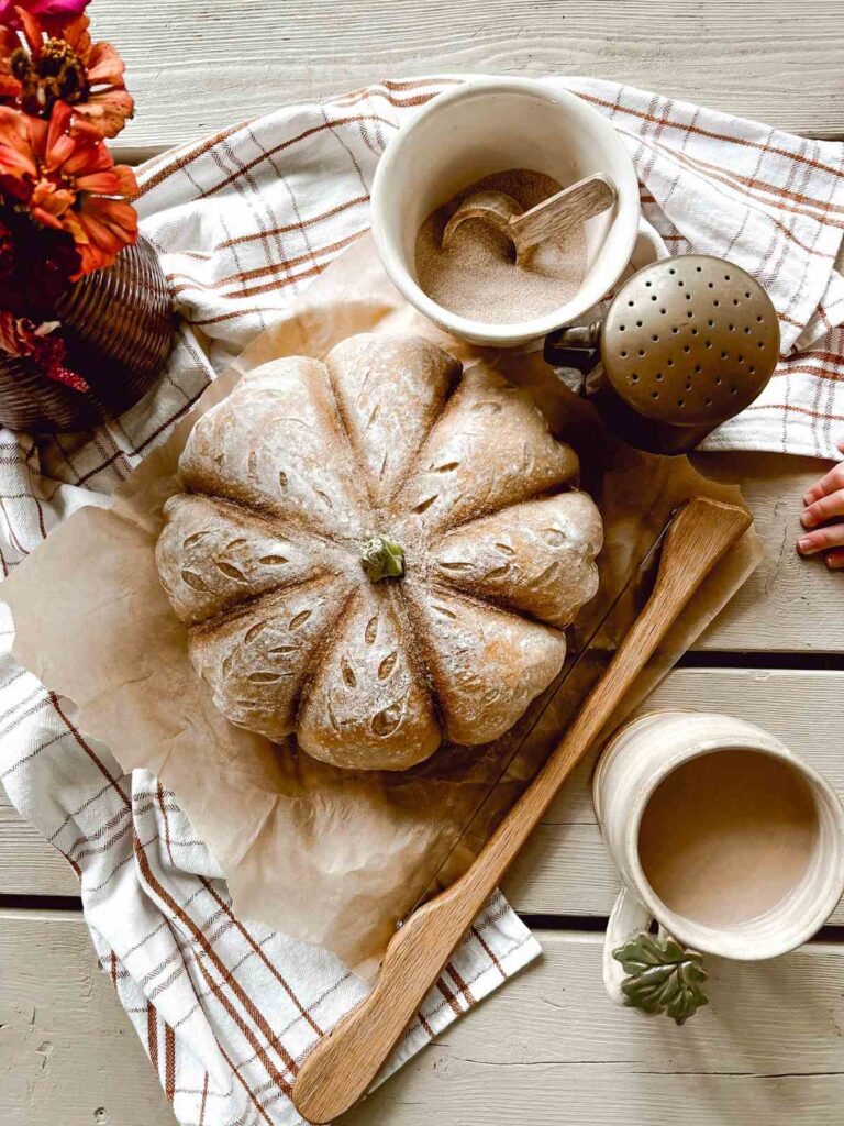 pumpkin-shaped sourdough loaf and coffee mug on table