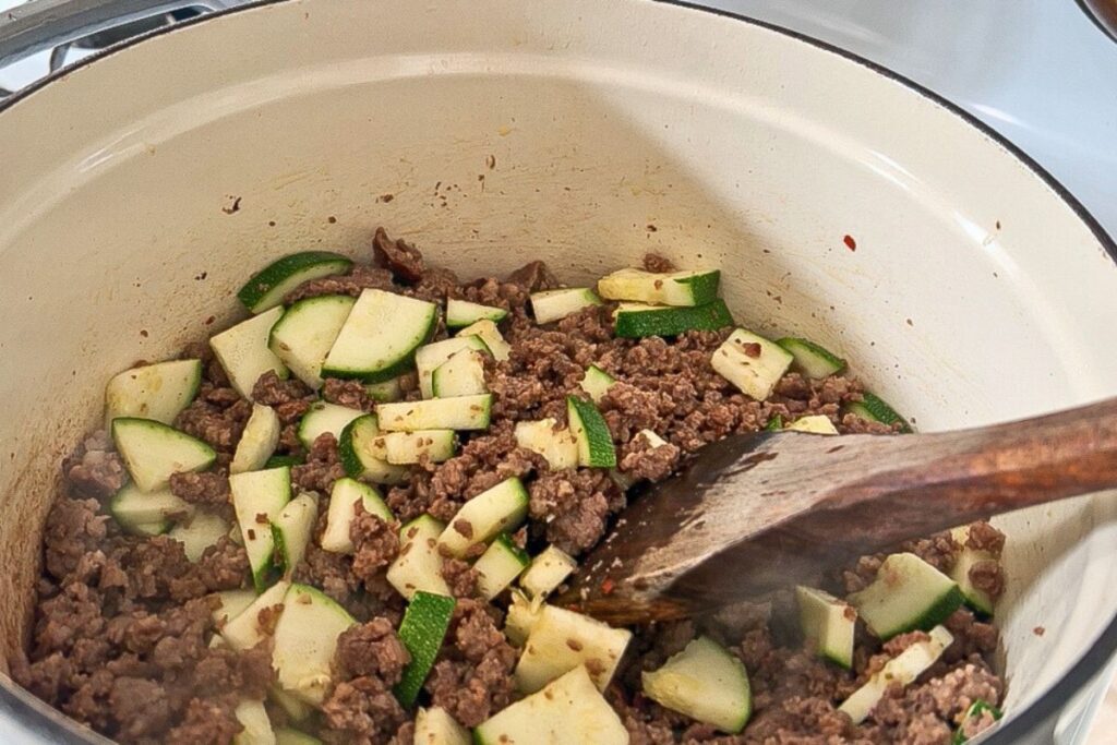 zucchini and sausage and onions frying in pan